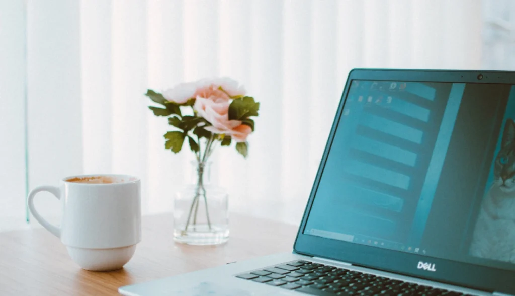 Notebook Dell Inspiron sobre mesa de trabalho ao lado de uma xícara de café, ideal para home office.
